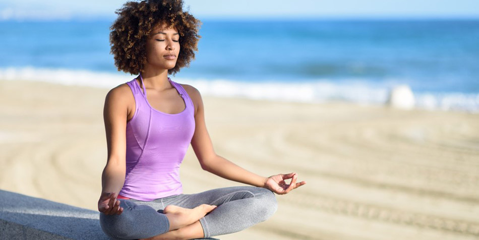 A woman meditates by the beach to reduce stress.